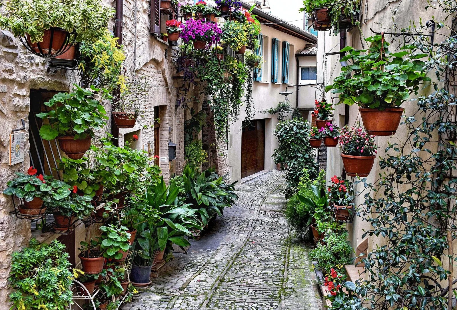 Un vicolo fiorito in pietra nel borgo medievale di Spello, con vasi di fiori su muri e balconi